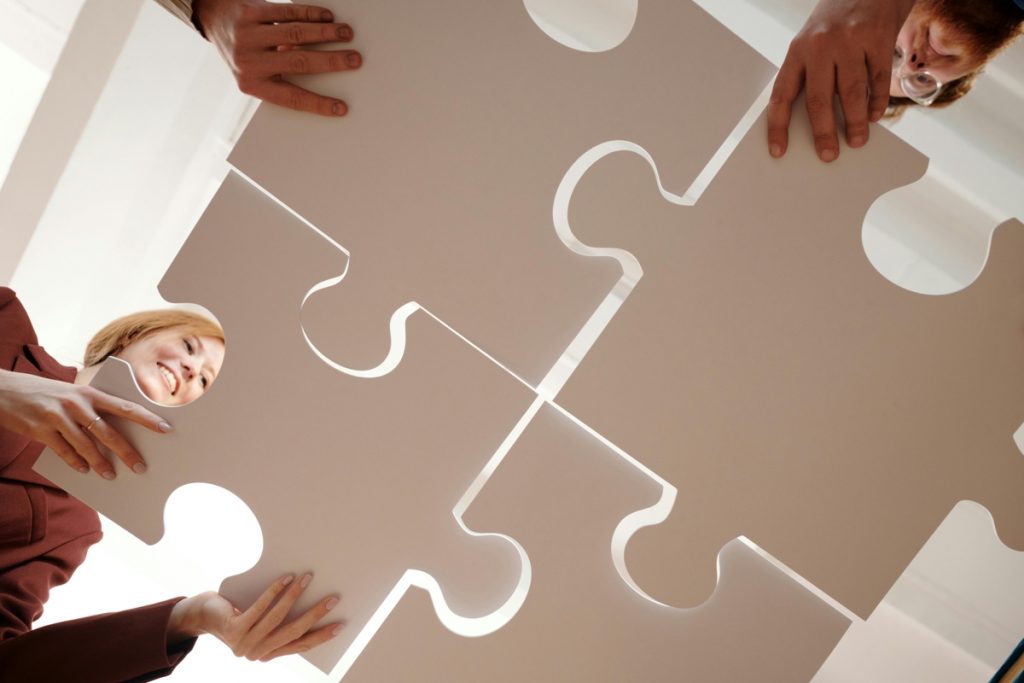 Team Putting a Puzzle Together Upward view from glass table of four people putting a puzzle together with four large pieces